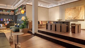 Eine moderne Lobby mit Empfangsschalter, Sitzgelegenheiten und einer Bücherwand mit Büchern und Pflanzen.