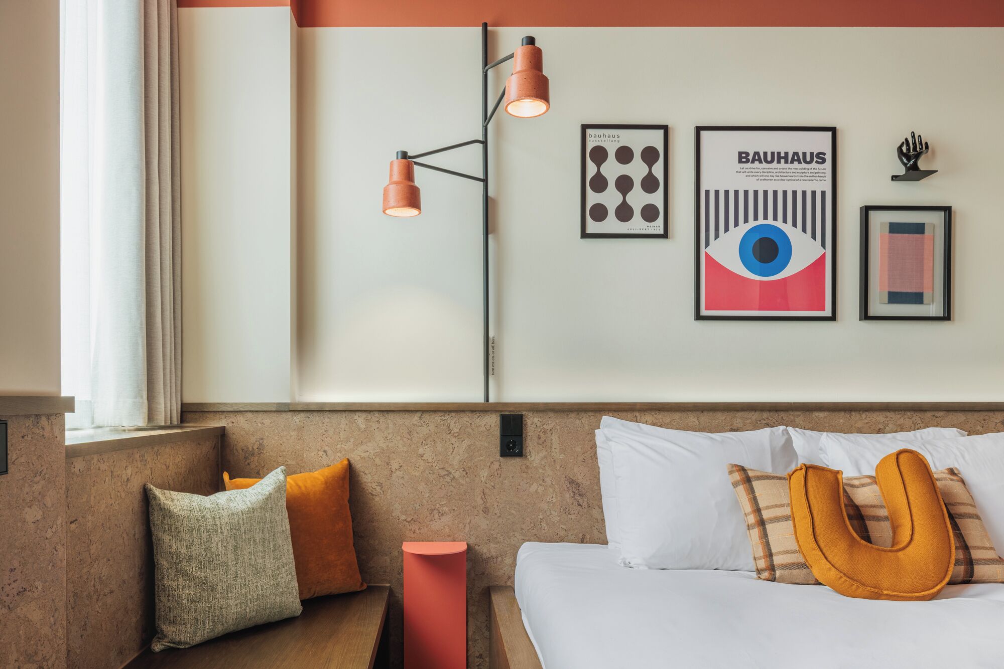 A hotel room with a bed, pillows, a nightstand, a wall-mounted lamp, and framed artwork.