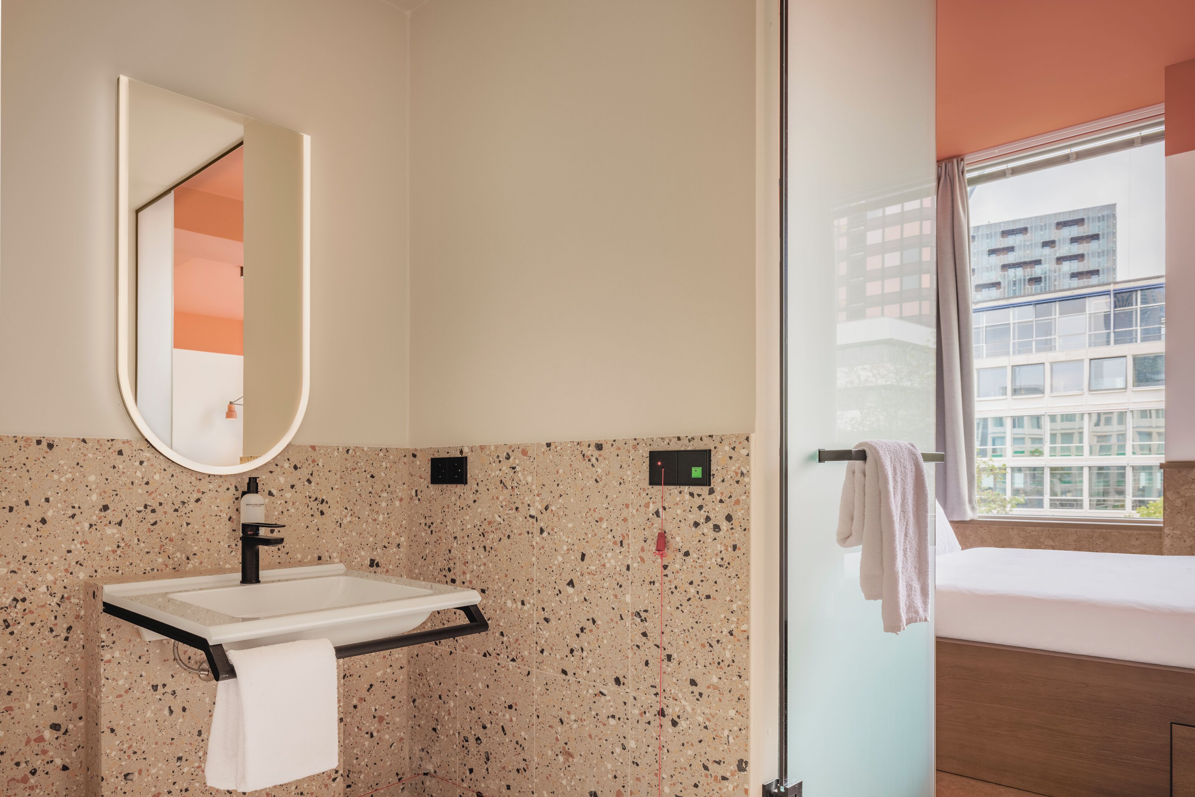 Un baño moderno con lavamanos de granito, un espejo y una ventana con vistas a edificios.