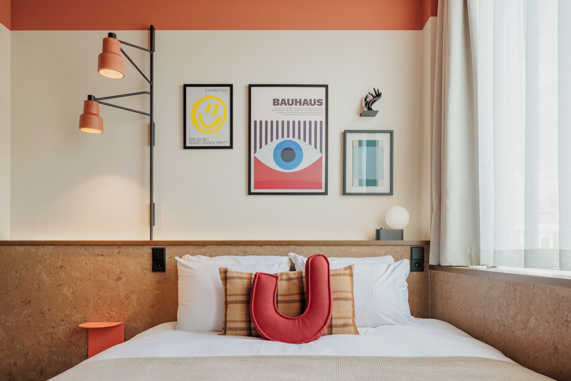 Une chambre d’hôtel avec un lit, des oreillers, un luminaire fixé au mur et des œuvres d’art encadrées.