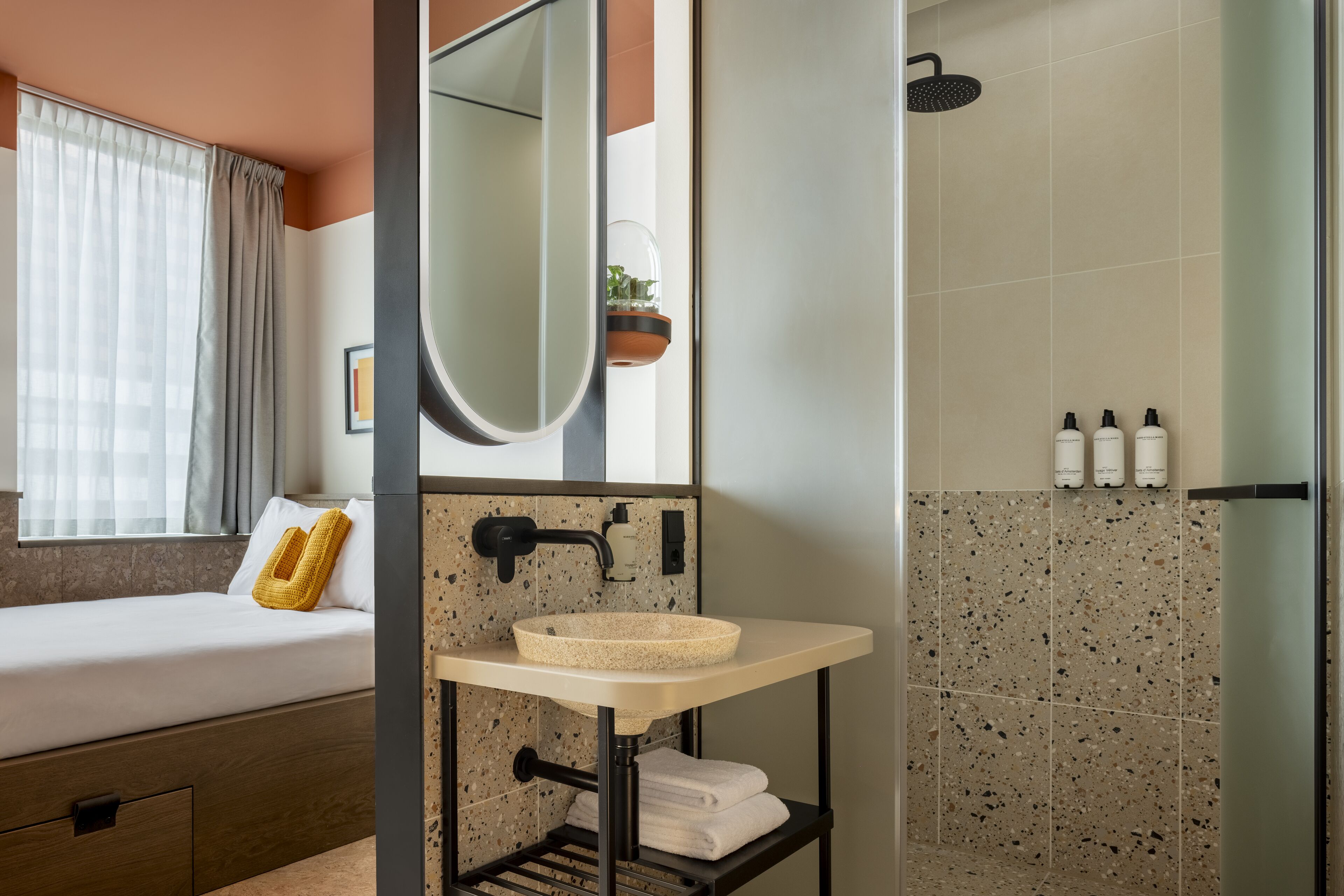 A modern bathroom with a freestanding sink, a shower, and a bed with a window.