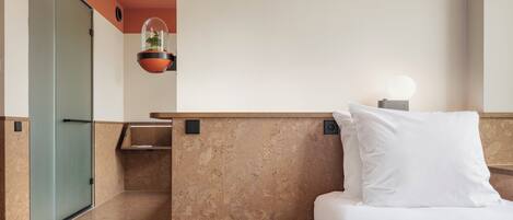 Ein Hotelzimmer mit Bett, Nachttisch, hängender Pflanze und kleinem Hocker.