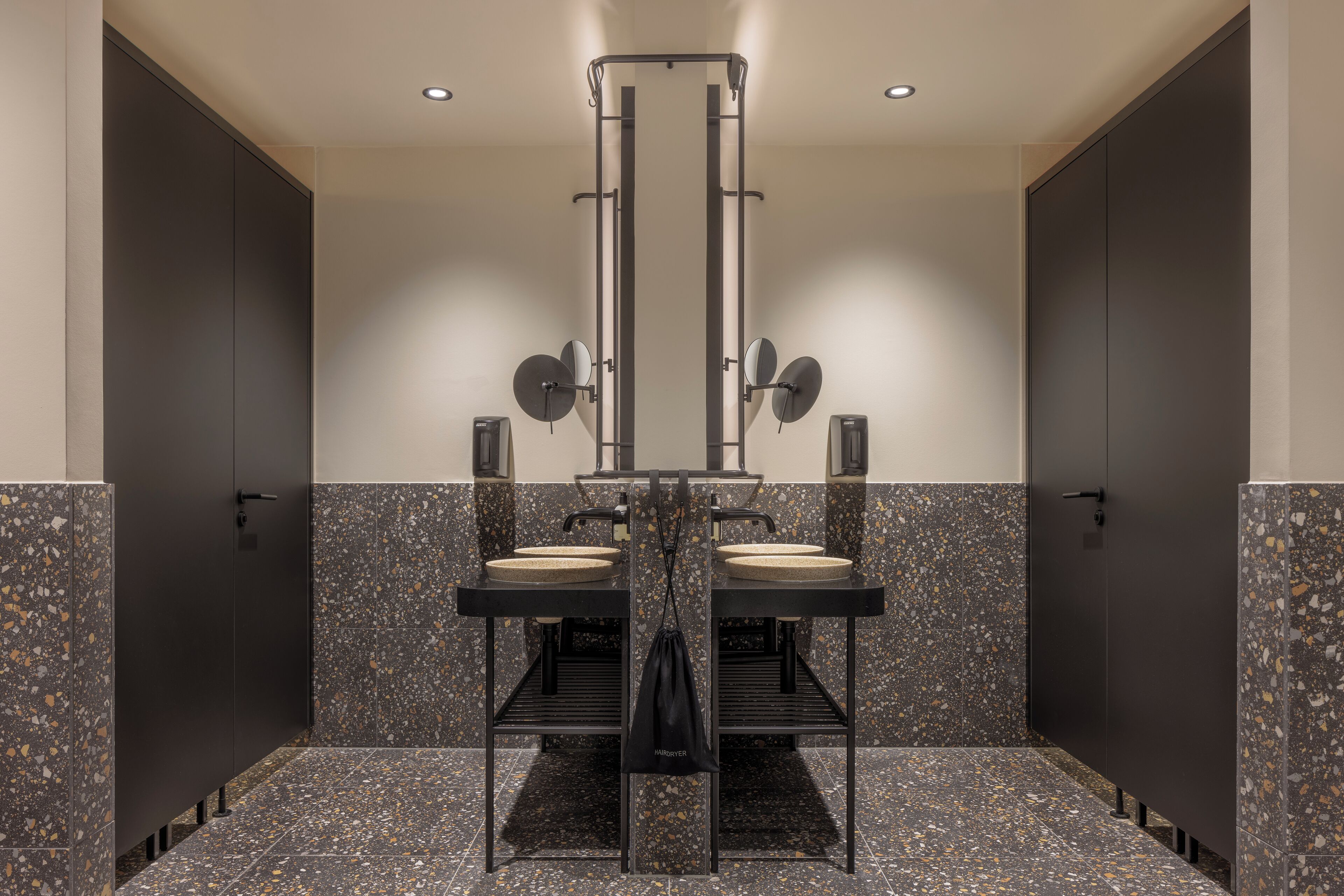 Eine öffentliche Toilette mit zwei Waschbecken, einem Händetrockner und einem Spiegel.