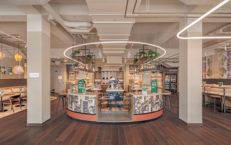A modern cafe with a central counter, seating areas, and a variety of baked goods displayed.