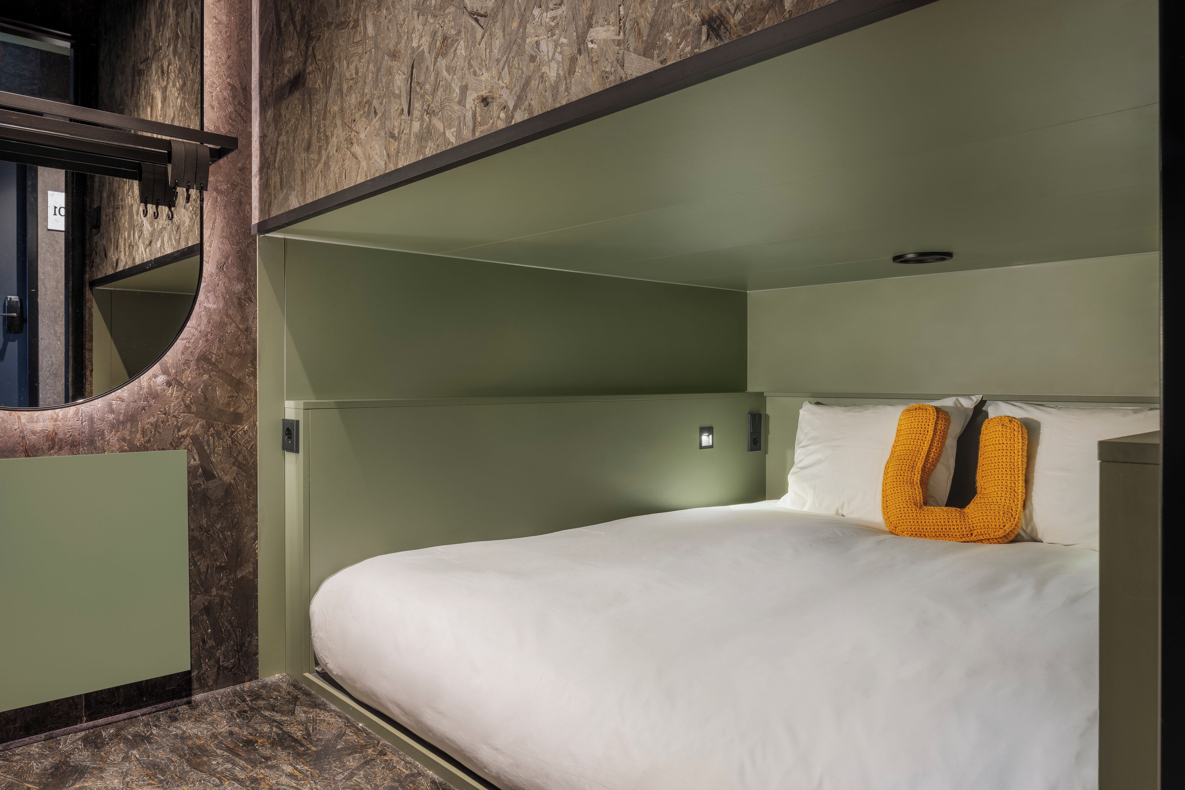 Habitación de hotel moderna con una pared curva, una cama con ropa blanca y una almohada naranja original.