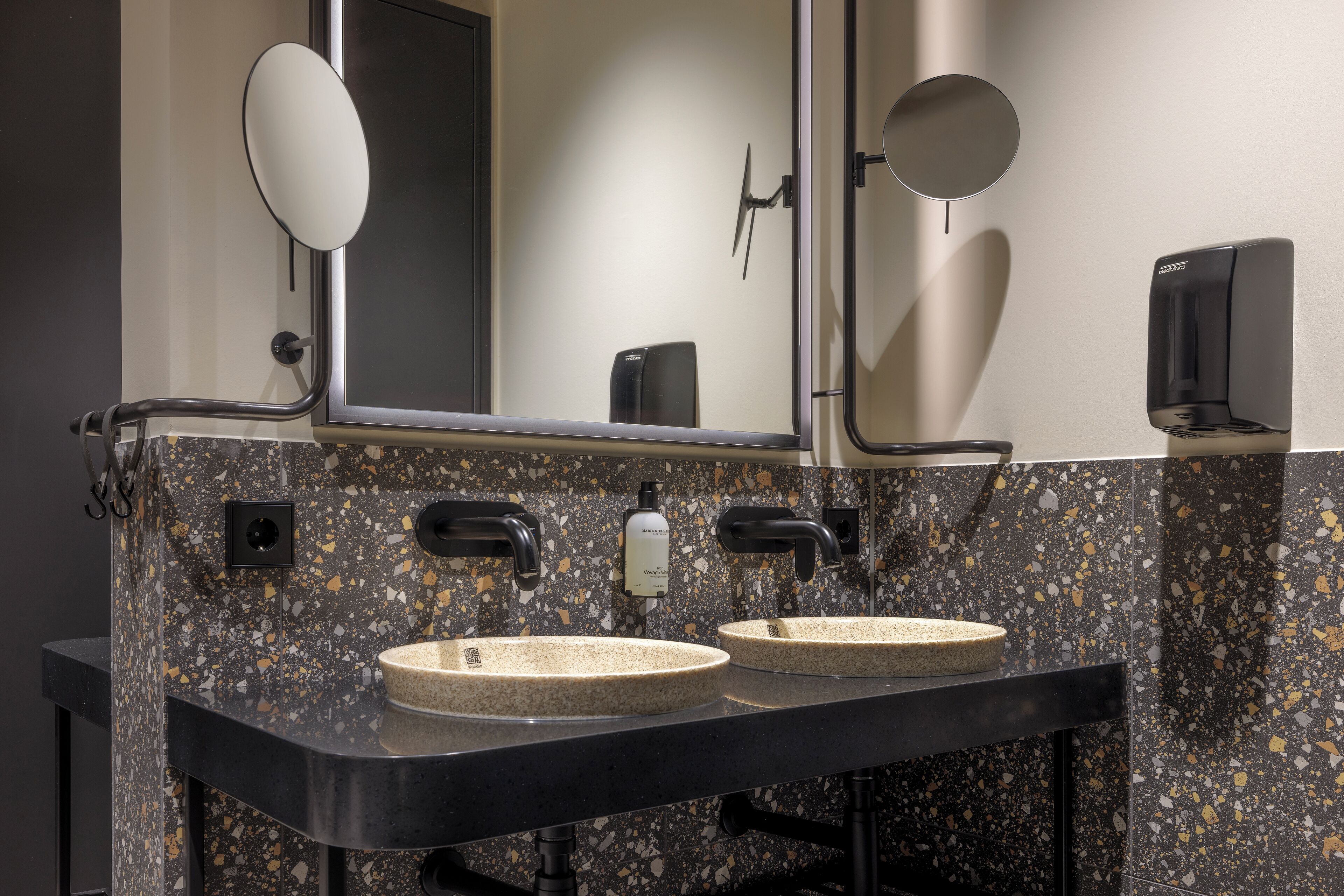 A modern bathroom with two sinks, a large mirror, and a soap dispenser.