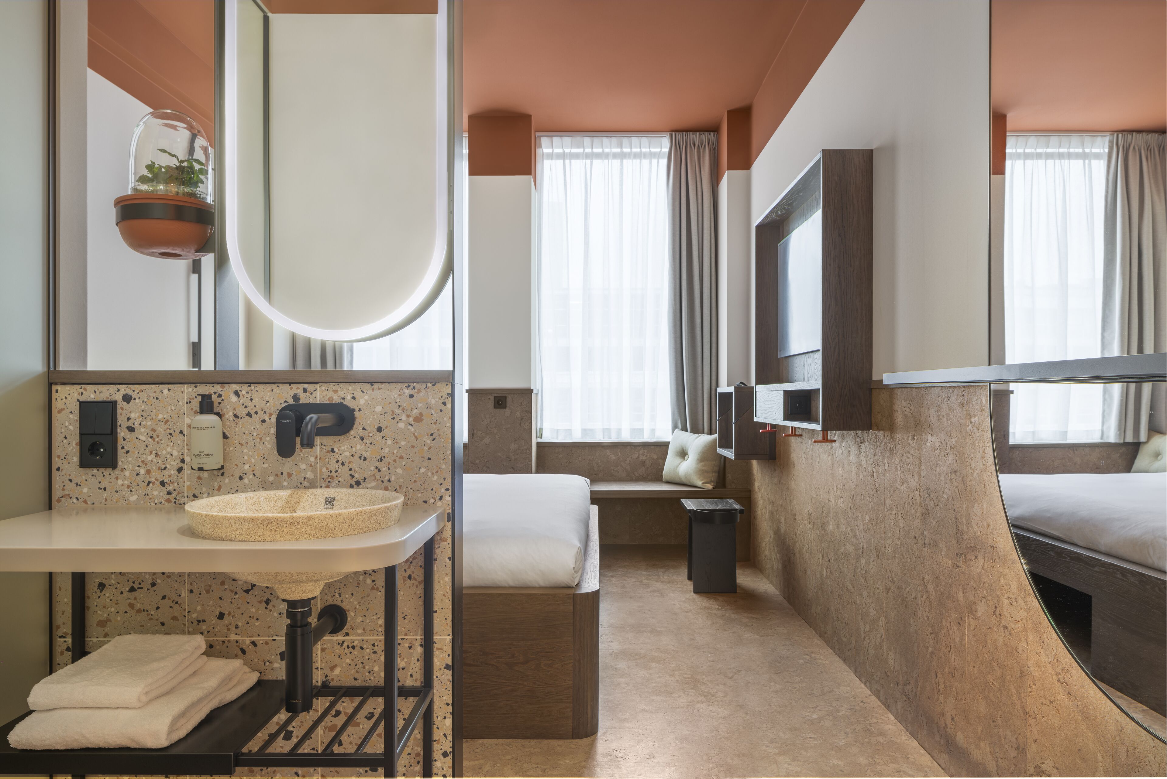 A modern bathroom with a round sink, a mirror, a towel rack, and a potted plant.