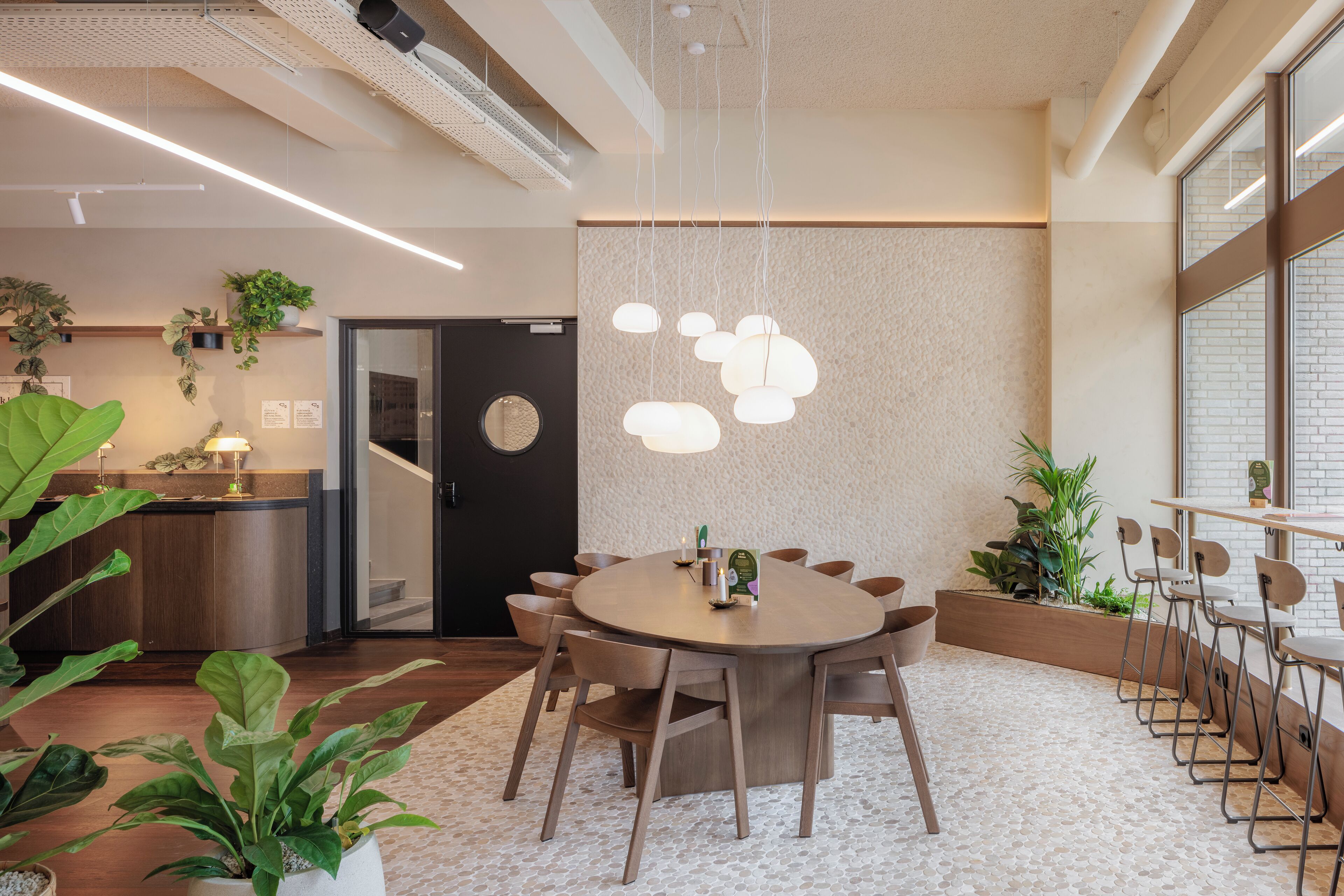 A modern conference room with a round table, chairs, hanging pendant lights, and potted plants.