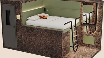 Une petite pièce comprenant un lit superposé, un petit bureau, une chaise, une échelle et un miroir.