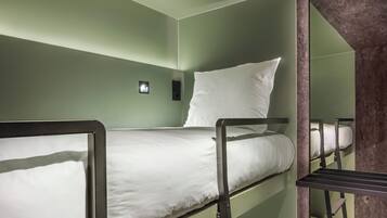 Ein Stockbett mit weißer Matratze und Kissen, einer kleinen Wandleuchte und einem dunkel gefärbten Metallrahmen.
