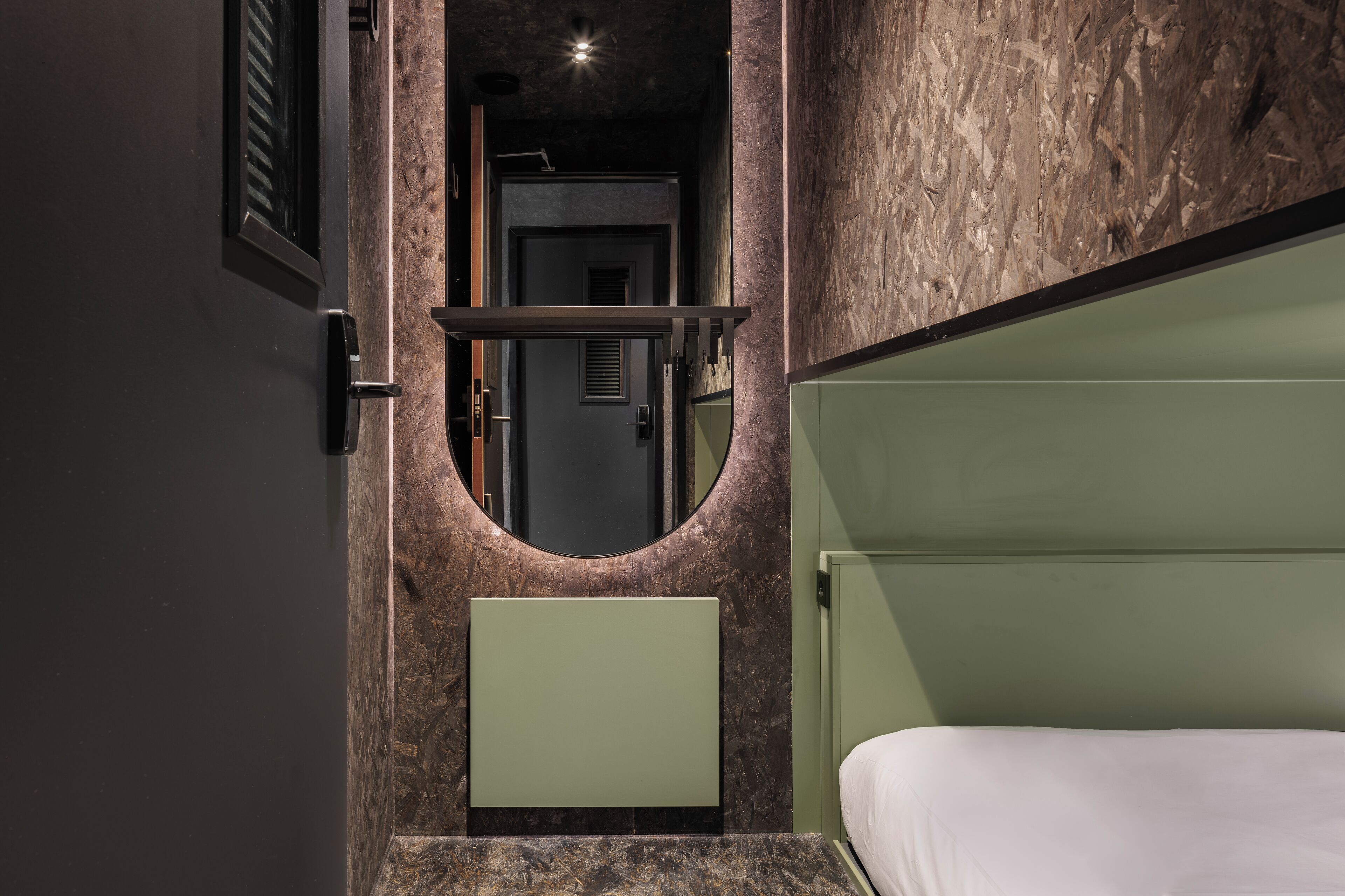 A modern bathroom with a marble wall, a green vanity, and a white bed.