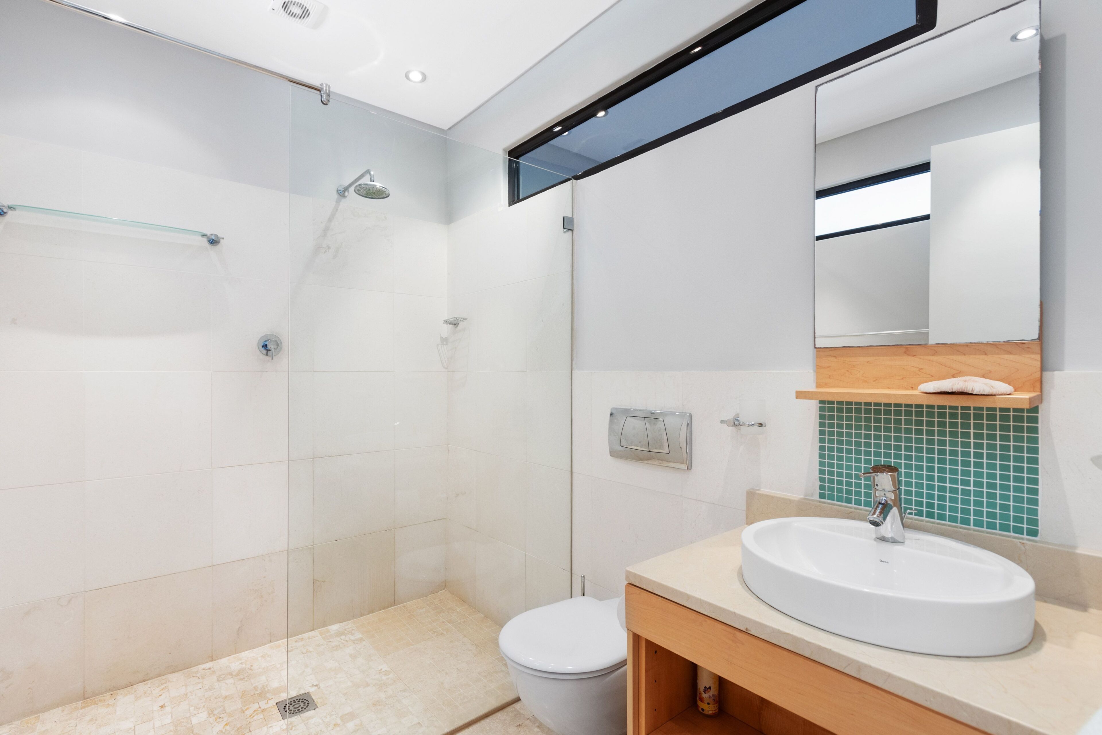 Un baño moderno con ducha envuelta en vidrio, inodoro blanco y lavamanos con tocador de madera.