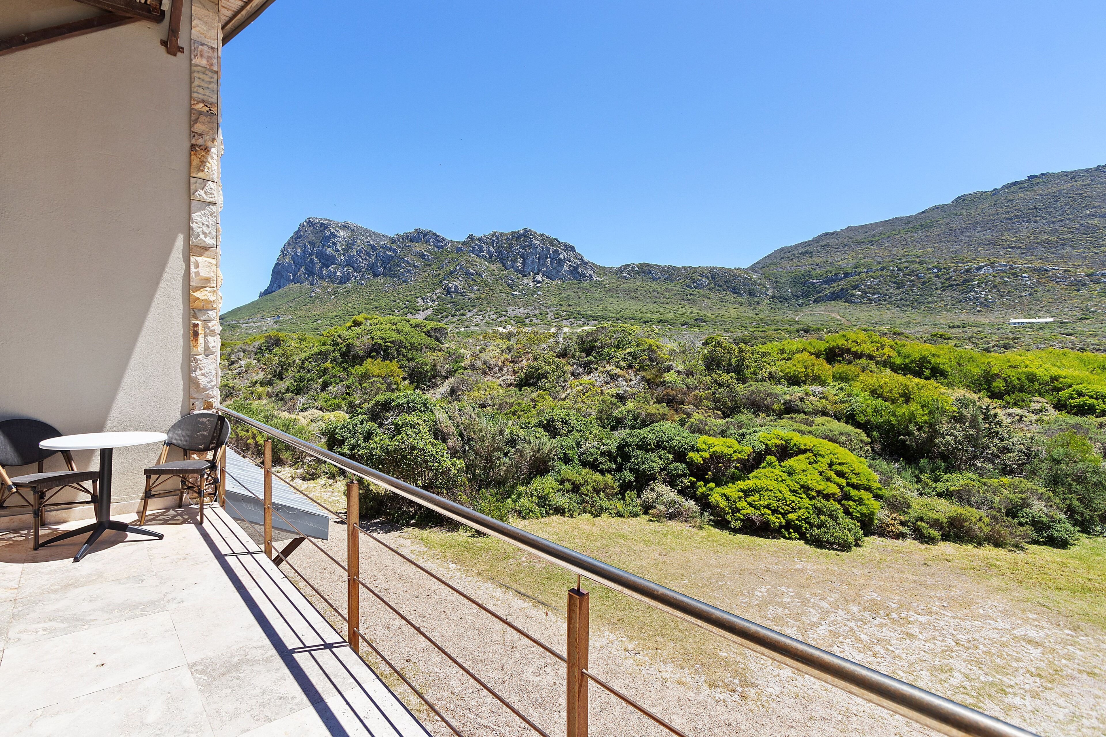 A balcony with a table and chairs, overlooking a mountainous landscape with greenery.