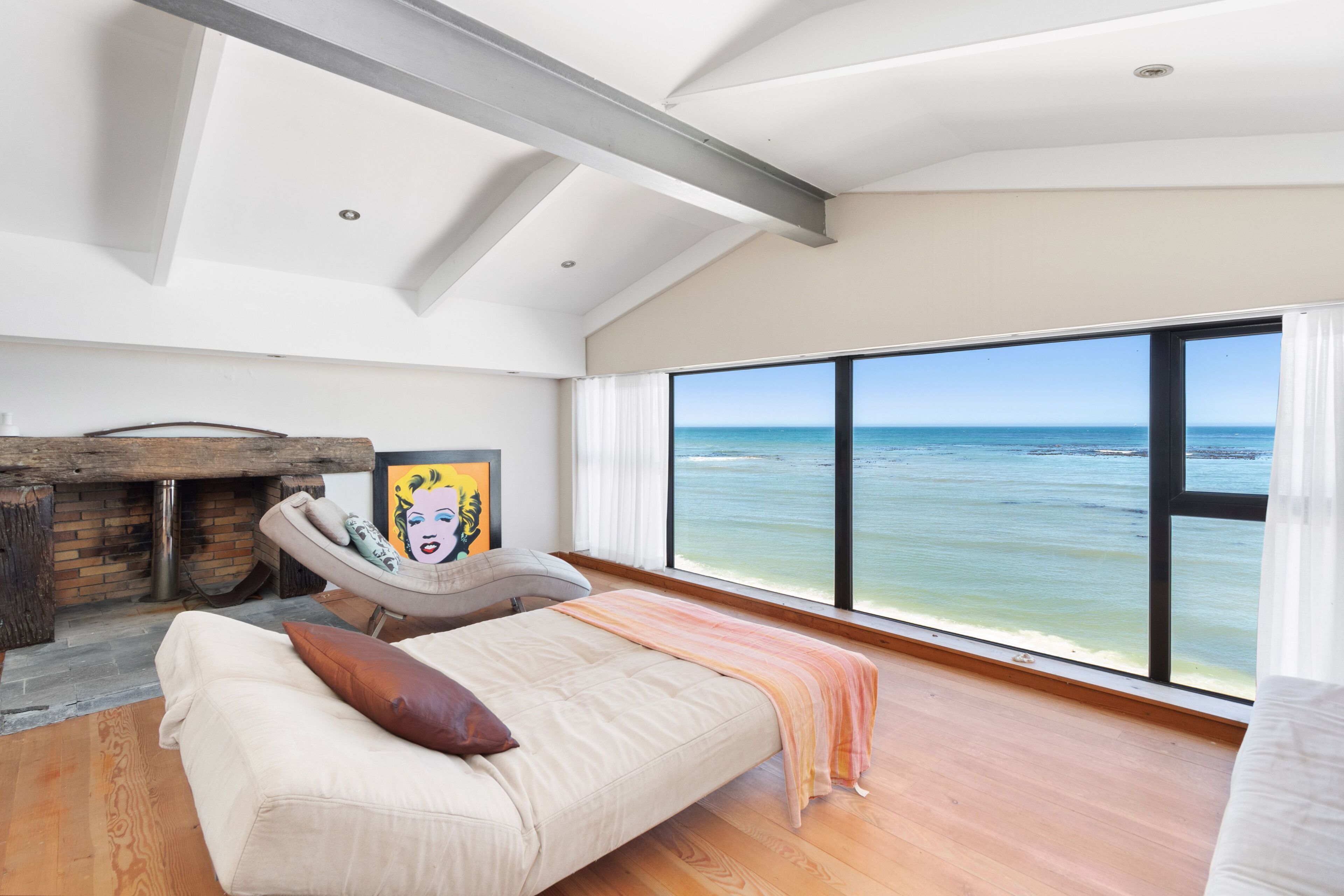 A bedroom with a large window overlooking the sea, a fireplace, and a modern design.