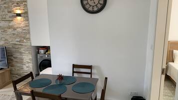 Un comedor con una mesa, sillas, un reloj, una lavadora y un pequeño cubo de basura.