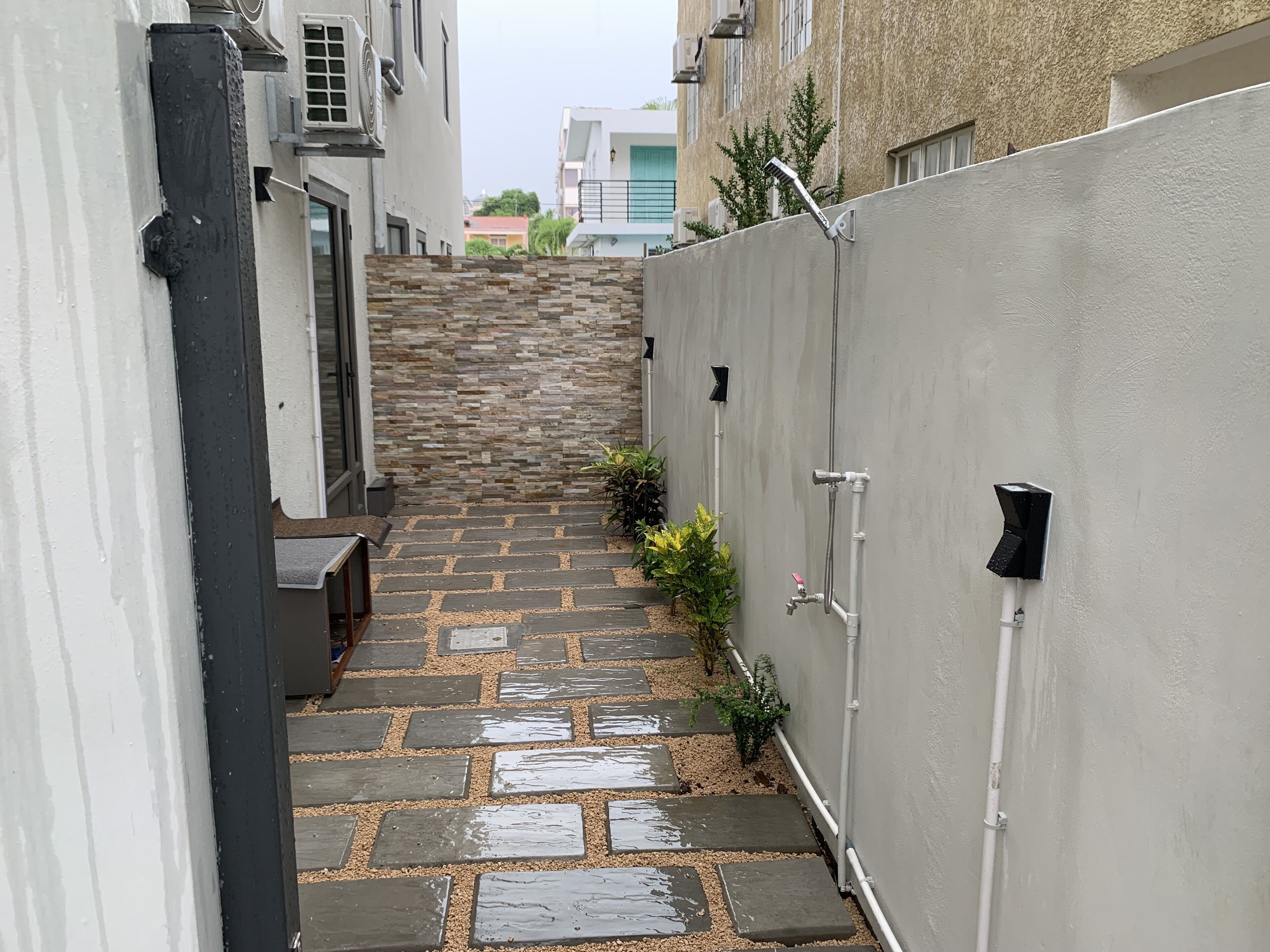 A narrow stone pathway leading up a set of steps in a residential area with white walls and a grey fence.