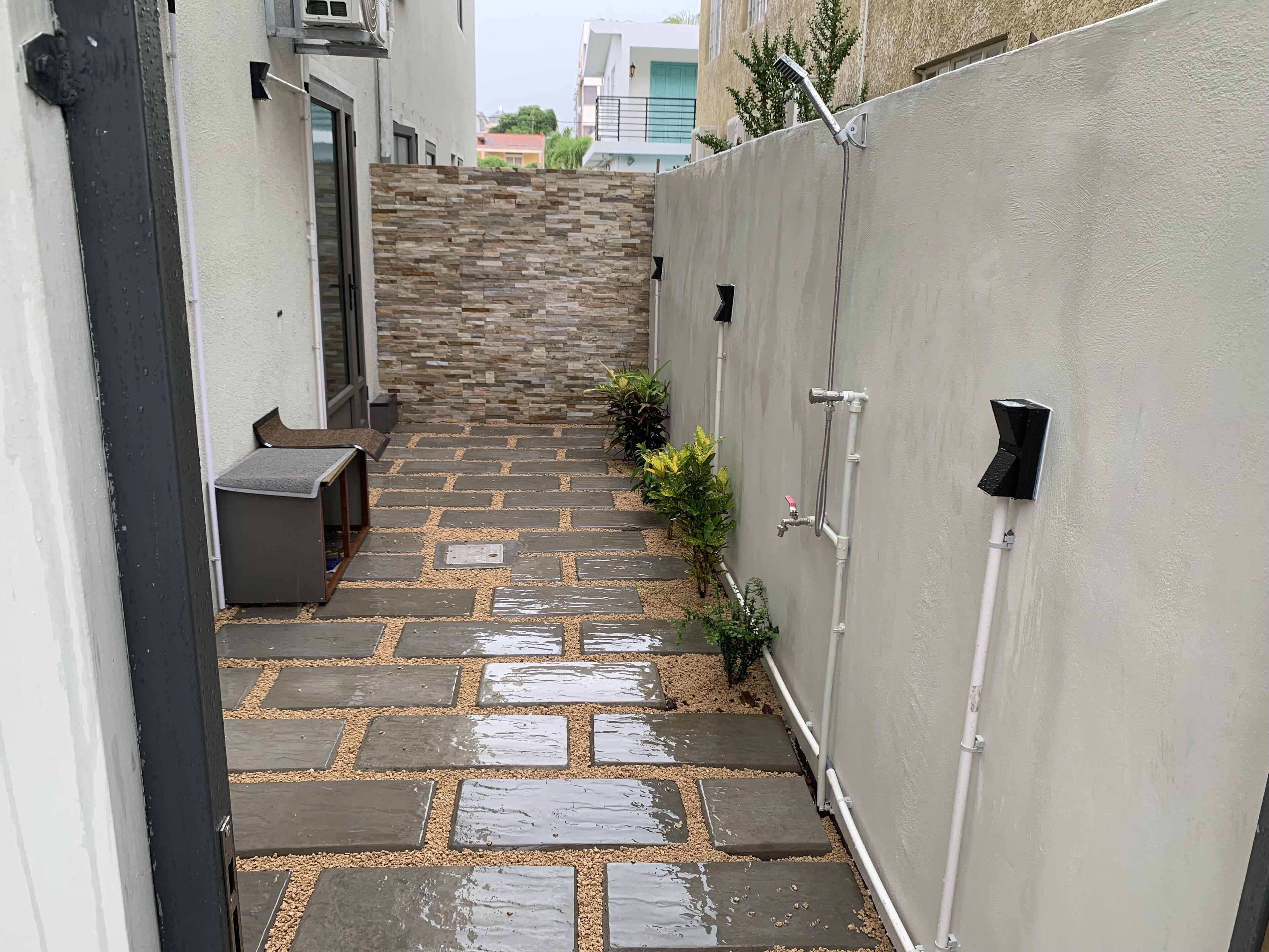 A narrow outdoor pathway with stone steps leading to a building entrance, surrounded by a low wall and potted plants.