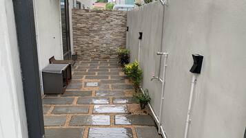 A narrow outdoor pathway with stone steps leading to a building entrance, surrounded by a low wall and potted plants.