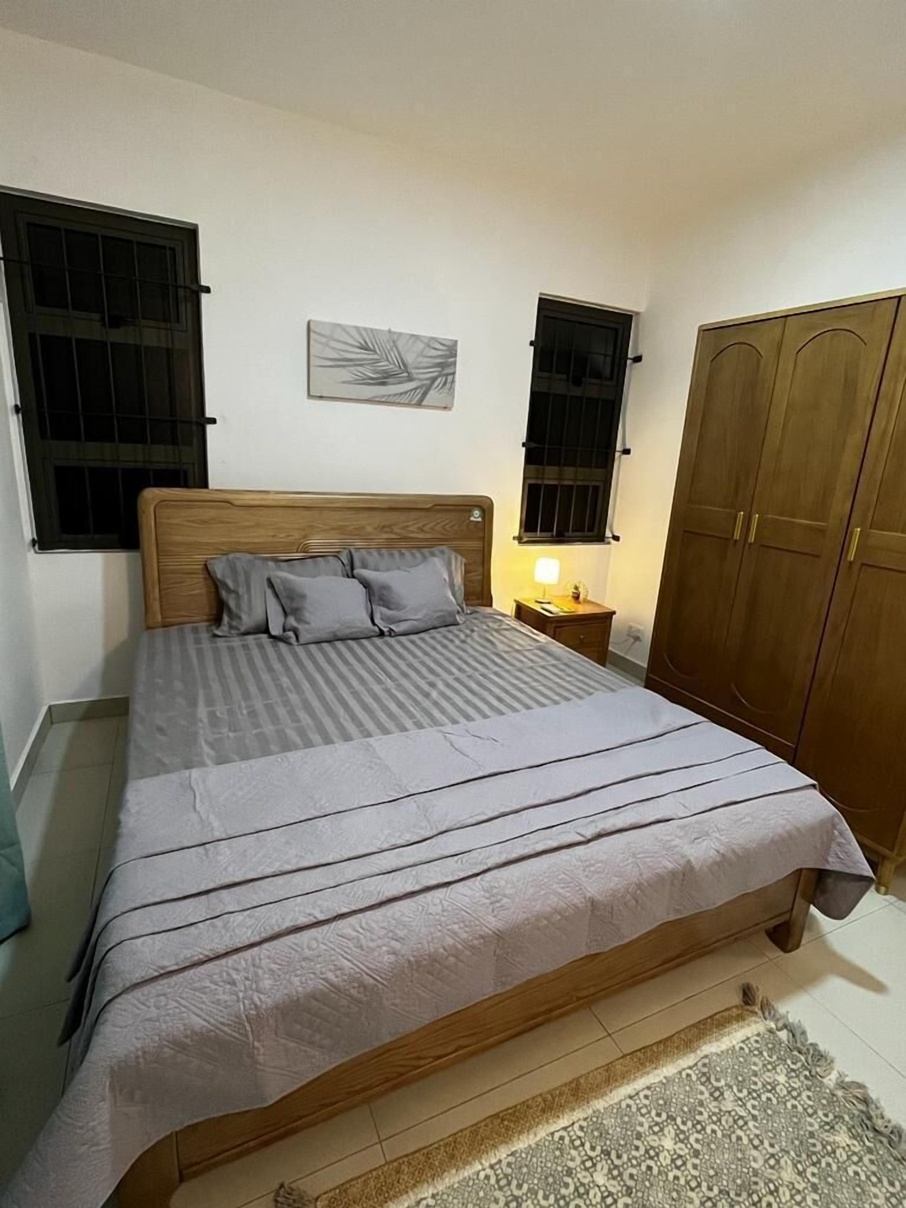 A bedroom with a wooden bed, two bedside tables, a nightstand, a wardrobe, and a wall-mounted artwork.