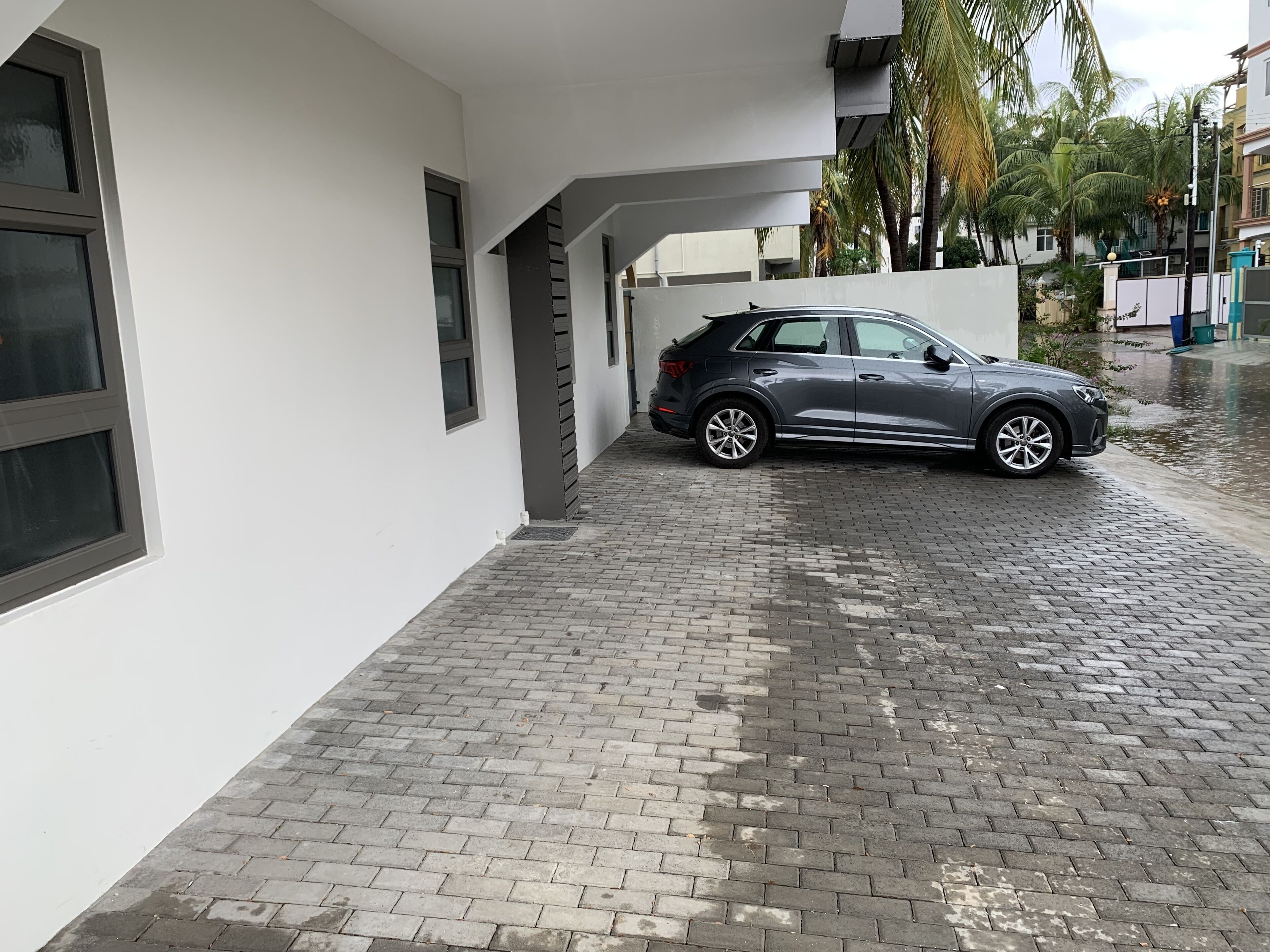 Un VUS gris est garé dans une allée abritée, devant un bâtiment blanc et un chemin pavé de briques.
