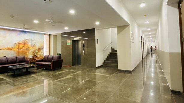 A spacious lobby with a marble floor, a seating area with sofas, a staircase, and a mural on the wall.