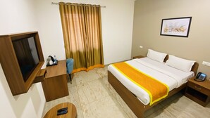 A hotel room with a bed, a desk, a chair, a TV, a bedside table, a nightstand, and a curtain.