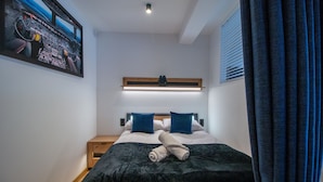 A modern hotel room with a neatly made bed, a small bedside table, a wall-mounted light, and a large window with curtains. - Apartament AVIATOR lokalizacja w centrum (Nowy Targ)