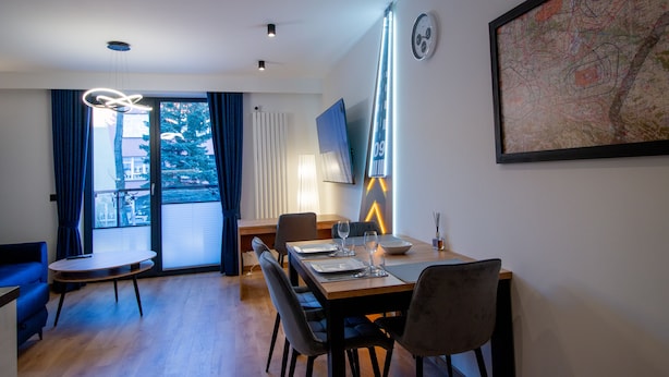 A modern dining area with a wooden table set for four, a blue sofa, and a large window with curtains. - Apartament AVIATOR lokalizacja w centrum (Nowy Targ)