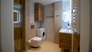 A compact bathroom with a toilet, washing machine, and wooden cabinets. - Apartament AVIATOR lokalizacja w centrum (Nowy Targ)