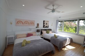 Ein Schlafzimmer mit zwei Betten, einem Deckenventilator und einem Fenster mit Blick auf Grünflächen.
