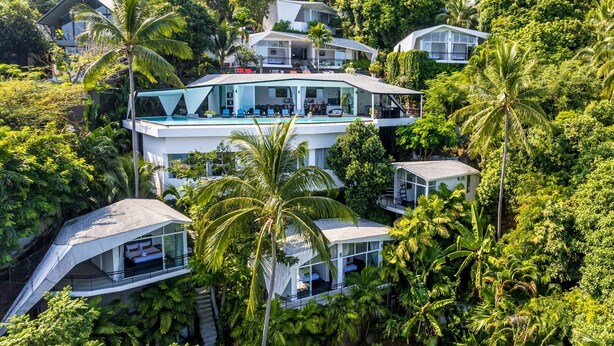 Een modern meerhoogpand omringd door weelderige begroeiing, met een groot glazen balkon en meerdere niveaus met buiten zitgedeeltes.