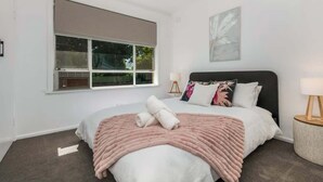 Une chambre moderne avec une grande fenêtre, un lit recouvert d’une couverture rose et une table de chevet avec une lampe.