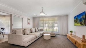 Un salon moderne avec un canapé d’angle beige, un pouf rond et une console en bois sur laquelle est posé un vase.