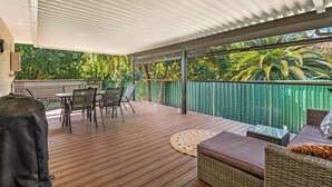 Un patio extérieur abrité, doté d’une terrasse en bois, de mobilier d’extérieur et offrant une vue sur une végétation luxuriante.