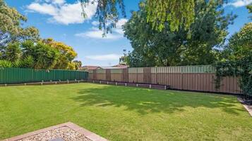 A backyard with a well-maintained lawn, a wooden fence, and a variety of trees.