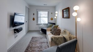 Ein modernes Wohnzimmer mit Flachbildfernseher, Deckenventilator, großem Fenster, Stehlampe und einer Couch mit Kissen.