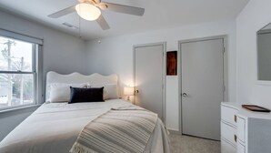 Ein Schlafzimmer mit einem Bett, einem Deckenventilator, einem Nachttisch, einer Kommode und einem Fenster.