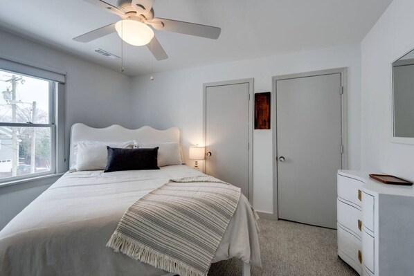 Un dormitorio con cama, ventilador de techo, mesita de noche, cómoda y ventana.