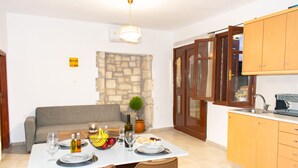 A dining area with a table set for two, a stone wall, a sofa, and wooden cabinets. - La Si'Ma, with private pool, 2-bedrooms close to Margarites Village (Plevriana)