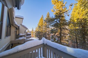 Un edificio residenziale con un balcone imbiancato dalla neve, circondato da alti alberi sempreverdi.