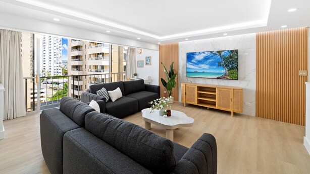 Ein modernes Wohnzimmer mit einem großen Flachbildfernseher, grauen Sofas, einem Couchtisch und einer Holztruhe.