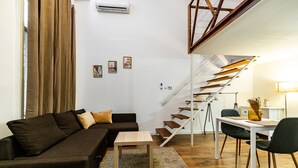 A modern living room with a brown sofa, a wooden coffee table, and a desk with a chair. A staircase with wooden steps leads to an upper level. - Venus Apartments - Keleti II (Budapest)