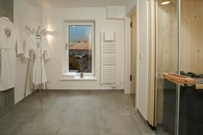 A modern bathroom with a window view, a glass shower enclosure, and a towel rack with robes.