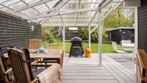 Eine überdachte Terrasse mit Holztisch und -stühlen, einem Grill und einer Gasflasche.