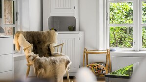 Ein gemütliches Zimmer mit Schaukelstuhl, kleinem Tisch und Fenster mit Blick ins Grüne.