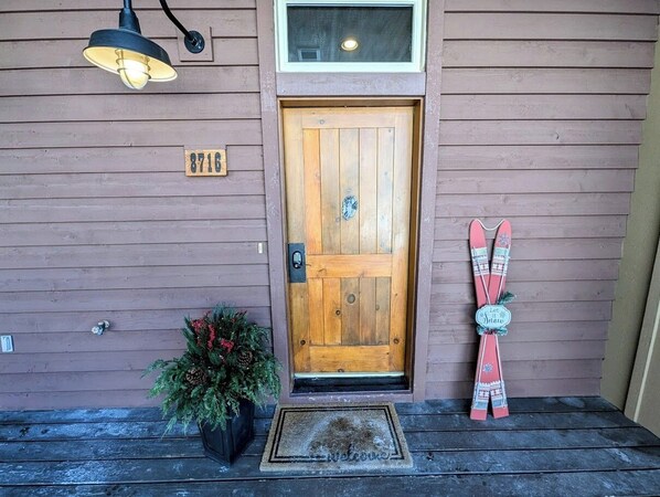 A wooden door with a mailbox and a number plate, a potted plant, and a decorative ski on the porch.