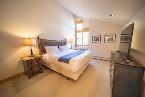 Quarto com cama, mesas de cabeceira, cômoda e janela.