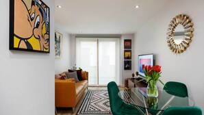 A modern living room with a glass dining table, green chairs, a sofa, and a large painting. - Old Town Chic, by Veeve (London)