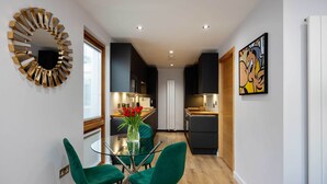 A modern kitchen with dark cabinetry, a glass dining table with green chairs, and a decorative mirror on the wall. - Old Town Chic, by Veeve (London)