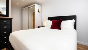 A neatly made bed with white and red pillows, a black headboard, and a wooden dresser with drawers. - Old Town Chic, by Veeve (London)